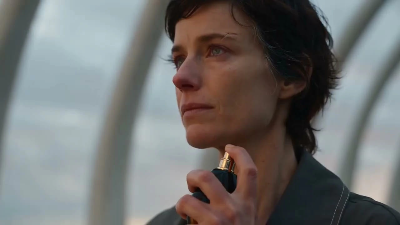 Close-up frame of a woman applying an AURENNE fragrance in a cosmetics commercial